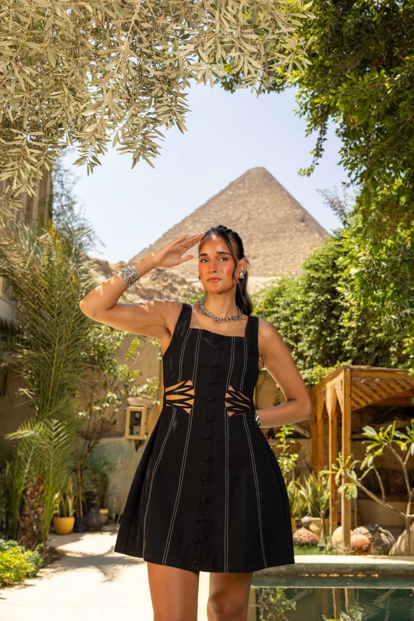 Woman in a black dress standing in a garden with a pyramid in the background Clep