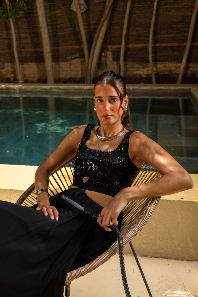 Woman in black sequin top sitting by a poolside Clep
