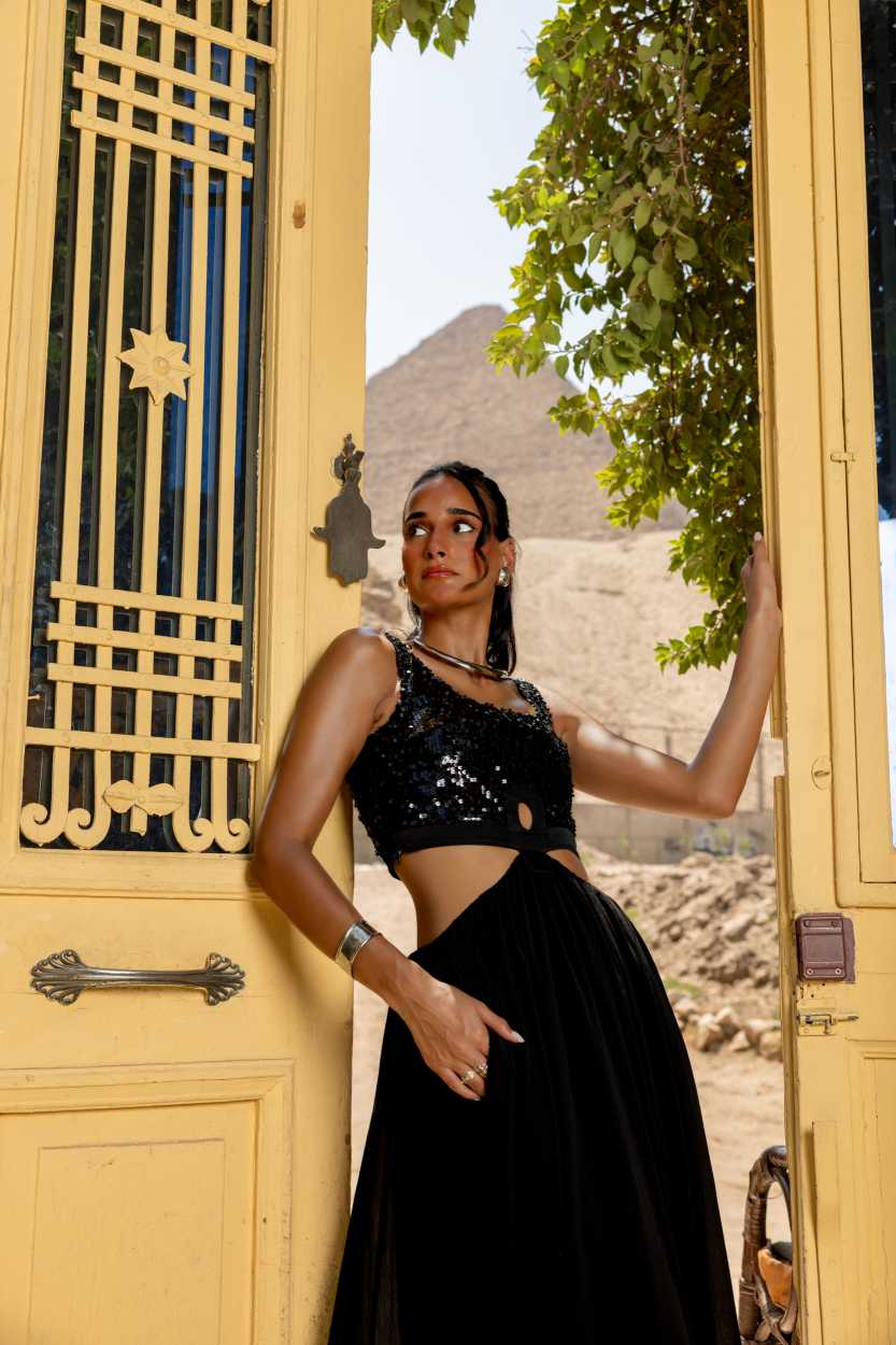Woman in a black outfit standing in front of a yellow door with a scenic background Clep
