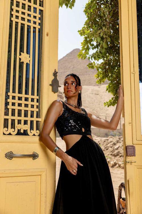 Woman in a black outfit standing in front of a yellow door with a scenic background Clep