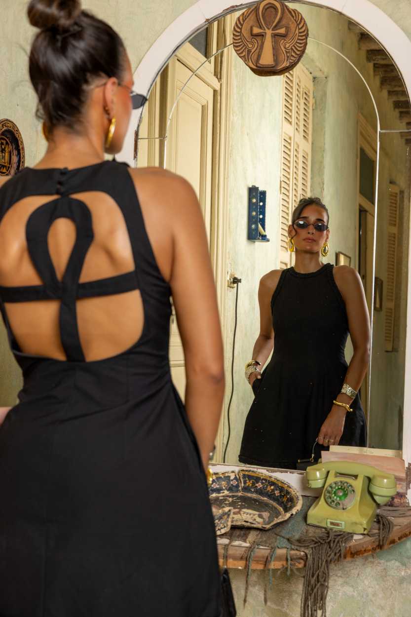 Woman in a black dress looking at herself in a mirror. Clep