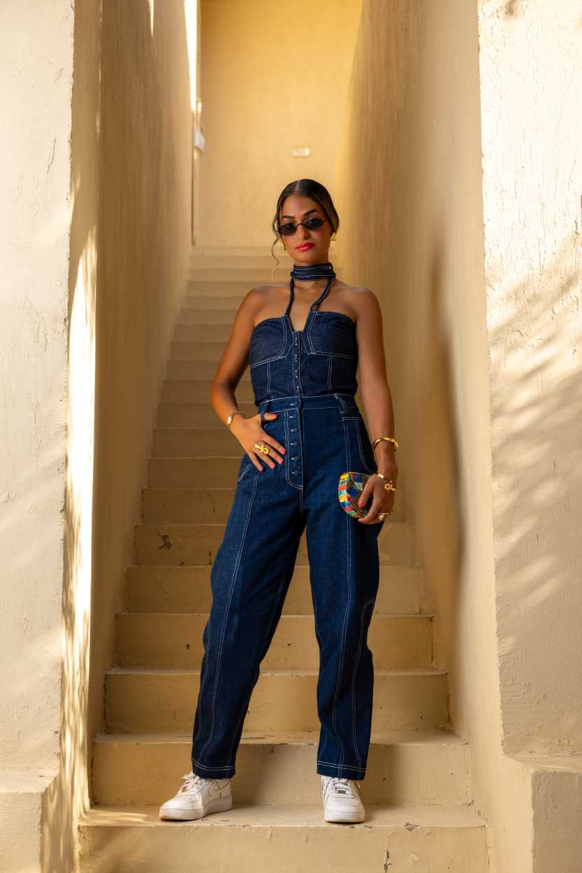 Woman in a denim jumpsuit standing on a staircase with warm lighting Clep