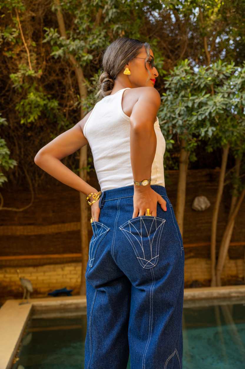 Woman in a white top and blue jeans standing by a pool with greenery in the background Clep