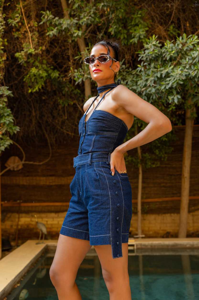 Woman wearing a blue denim outfit standing by a pool with greenery in the background Clep