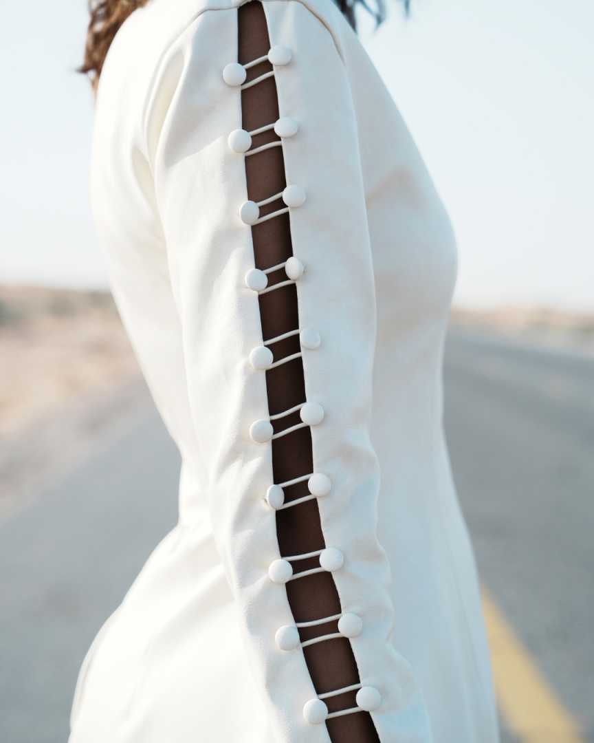 Close-up of a white garment with button details on a blurred outdoor background Clep