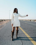 Person in a white dress and brown boots standing on an empty road Clep