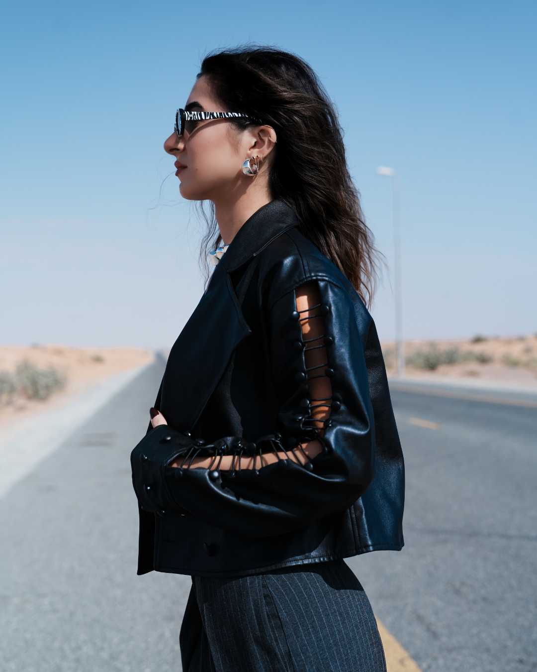 Woman wearing a black leather jacket with cut-out sleeves on a desert road. Clep