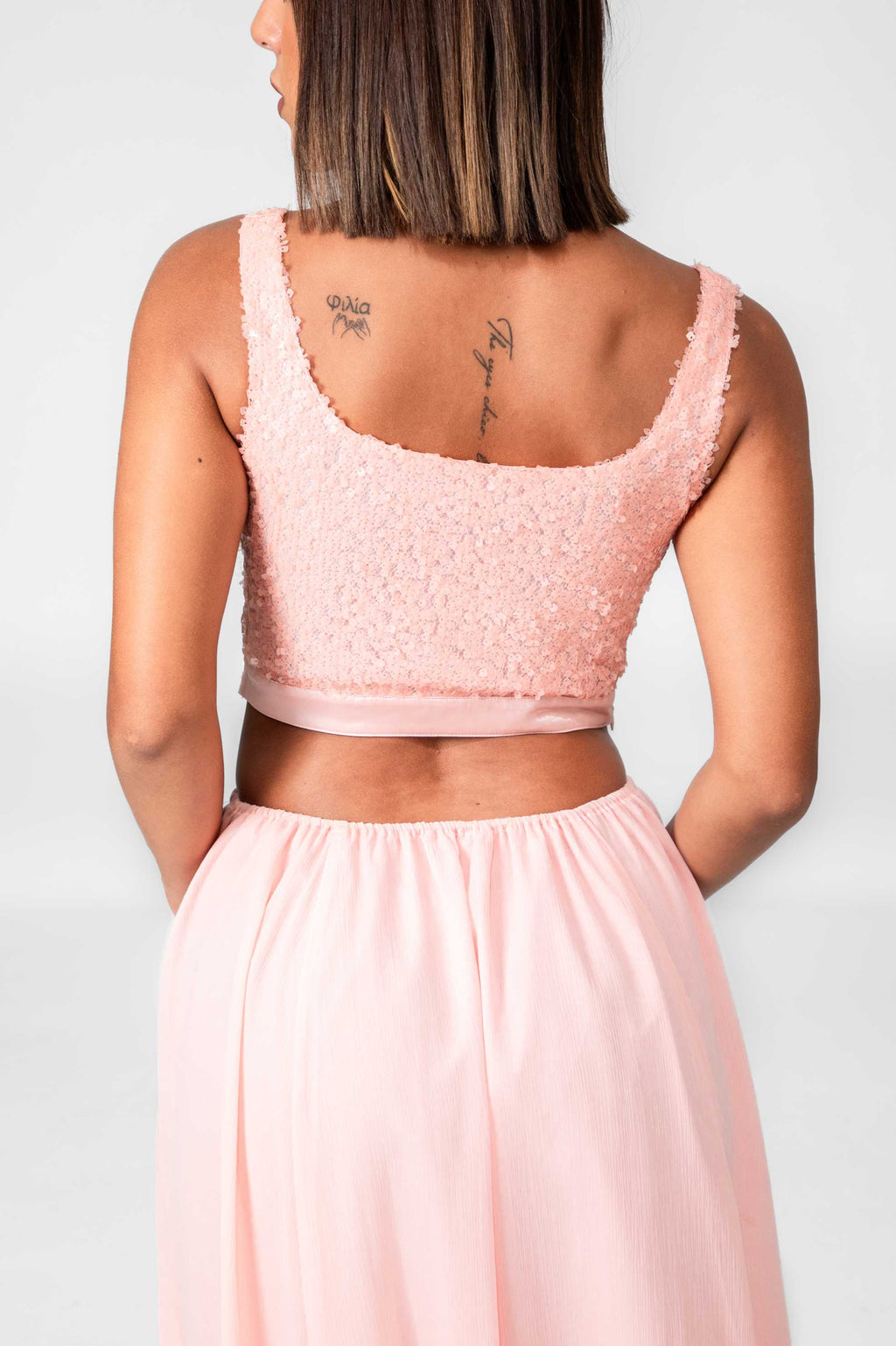 Woman wearing a pink lace top and skirt set against a white background Clep