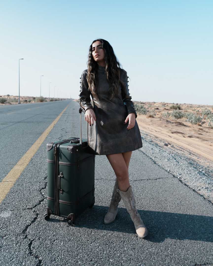 Woman standing on a desert road with a suitcase Clep