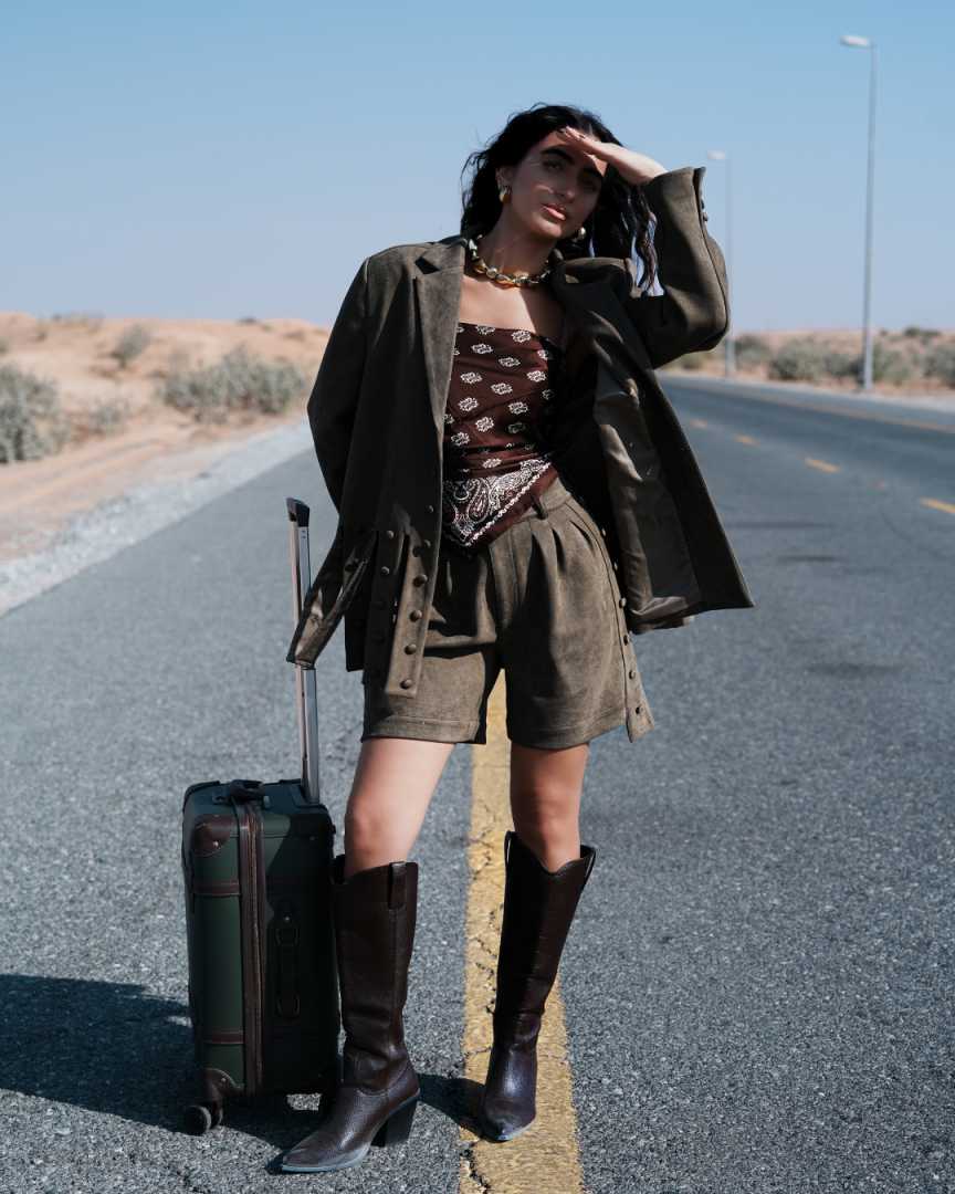 Woman in a desert setting with a suitcase, wearing a brown outfit. Clep