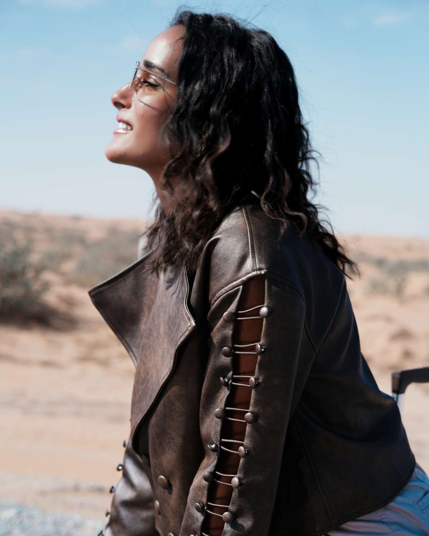 Woman wearing a brown leather jacket with decorative elements in a desert setting Clep