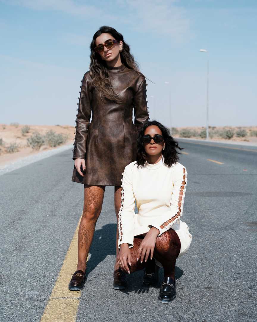 Two women in stylish outfits standing on a desert road. Clep