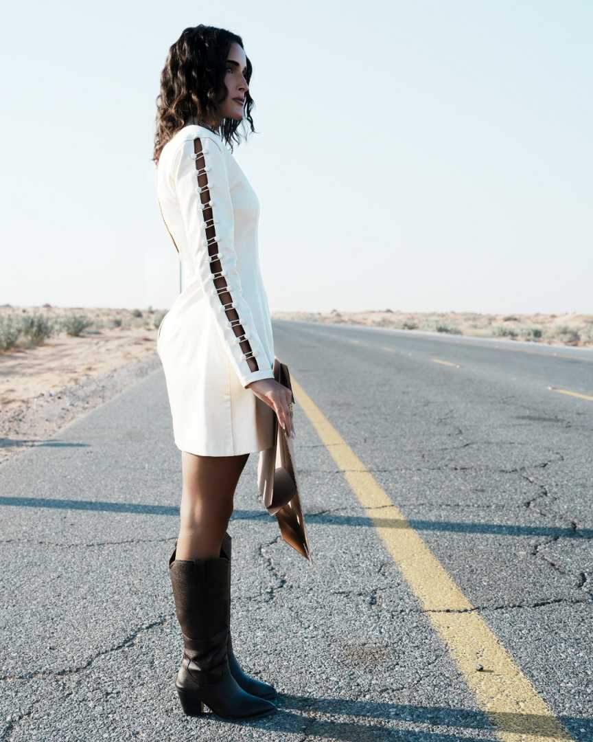Woman in a white dress and brown boots standing on a desert road Clep