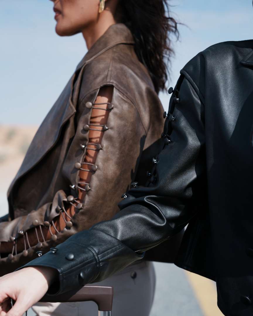 Close-up of a person wearing a brown leather jacket with intricate designs, standing outdoors. Clep